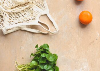 three oranges and a bag of greens on a table