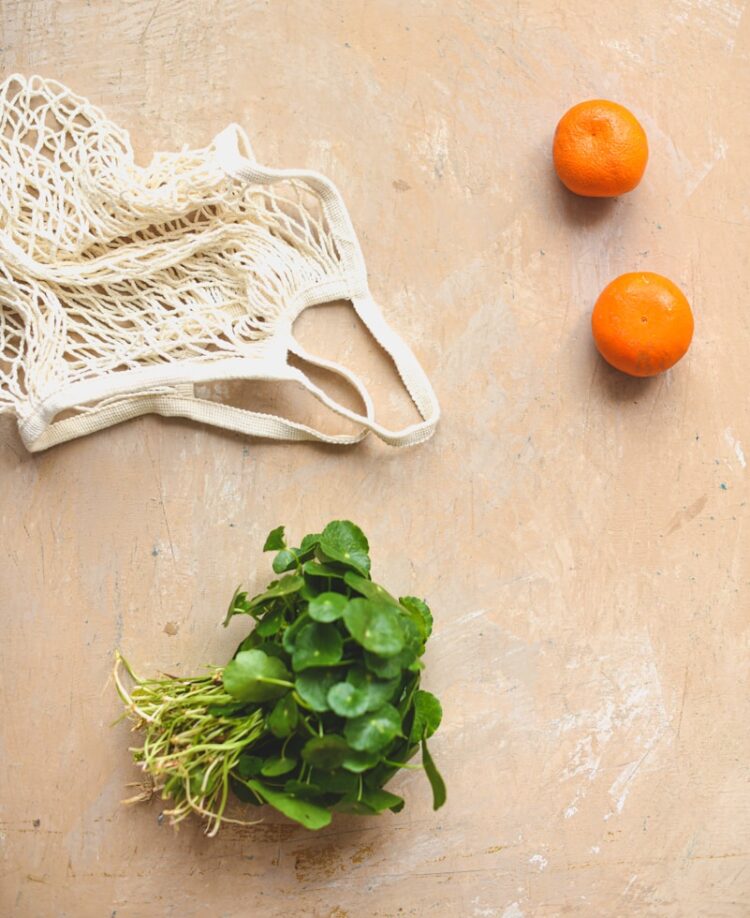three oranges and a bag of greens on a table