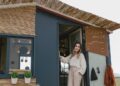 Woman in boho attire standing by a mobile tiny house surrounded by nature.