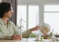 A young woman explores renewable energy with a globe and wind turbine model indoors.
