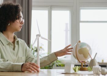 A young woman explores renewable energy with a globe and wind turbine model indoors.