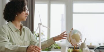 A young woman explores renewable energy with a globe and wind turbine model indoors.