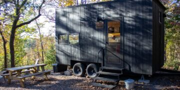 A dark tiny house with a picnic table outside.
