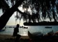 A person sits on a swing near the beach.