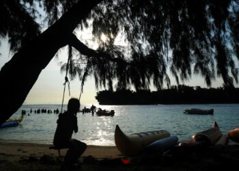 A person sits on a swing near the beach.