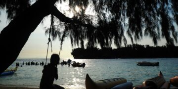 A person sits on a swing near the beach.