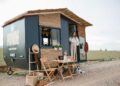Woman standing by a stylish mobile home in an open field, ideal for travel enthusiasts.