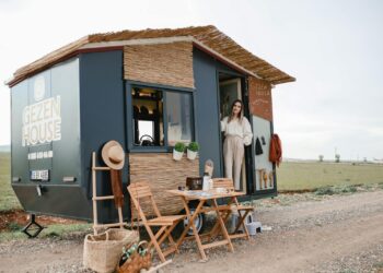 Woman standing by a stylish mobile home in an open field, ideal for travel enthusiasts.