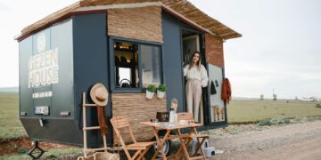 Woman standing by a stylish mobile home in an open field, ideal for travel enthusiasts.