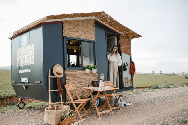Woman standing by a stylish mobile home in an open field, ideal for travel enthusiasts.