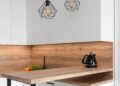 Interior of modern white kitchen with timber table and metal geometrical glowing lamps