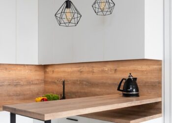 Interior of modern white kitchen with timber table and metal geometrical glowing lamps