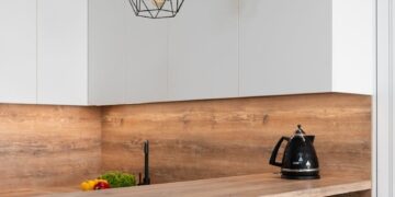 Interior of modern white kitchen with timber table and metal geometrical glowing lamps