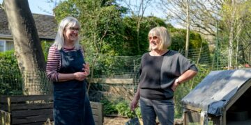 Smiling senior women enjoying gardening in a sunny backyard garden setting.