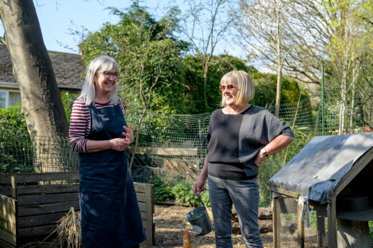 Smiling senior women enjoying gardening in a sunny backyard garden setting.