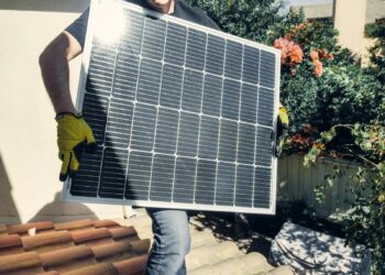 Technician carrying solar panel on rooftop. Clean energy installation outdoors.