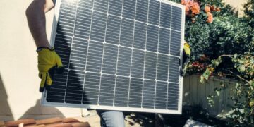 Technician carrying solar panel on rooftop. Clean energy installation outdoors.