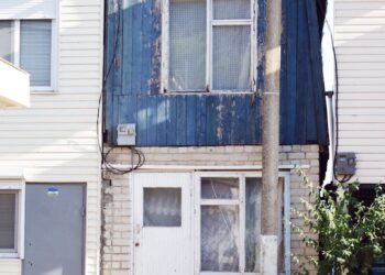 A small, rustic blue house exterior with visible wear, capturing urban character.