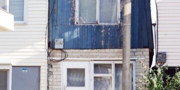 A small, rustic blue house exterior with visible wear, capturing urban character.