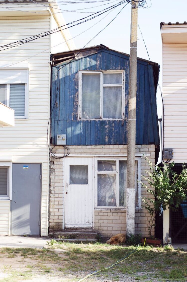 A small, rustic blue house exterior with visible wear, capturing urban character.