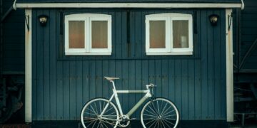 white and blue city bike parked beside gray wooden house
