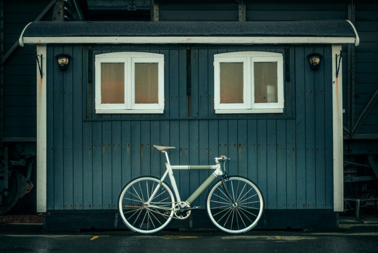 white and blue city bike parked beside gray wooden house