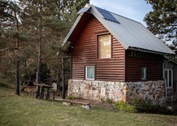 Charming wooden cabin in a tranquil countryside with trees and open sky.