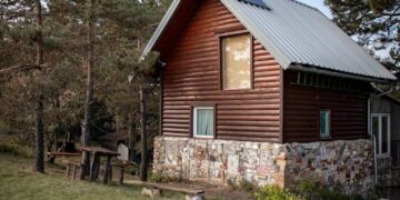 Charming wooden cabin in a tranquil countryside with trees and open sky.
