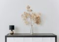 A stylish minimalist interior with a floral arrangement and a sleek lamp on a wooden table.