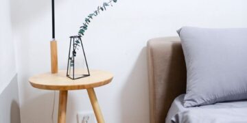 Modern minimalist bedroom with wooden nightstand, sleek lamp, and gray bedding set.