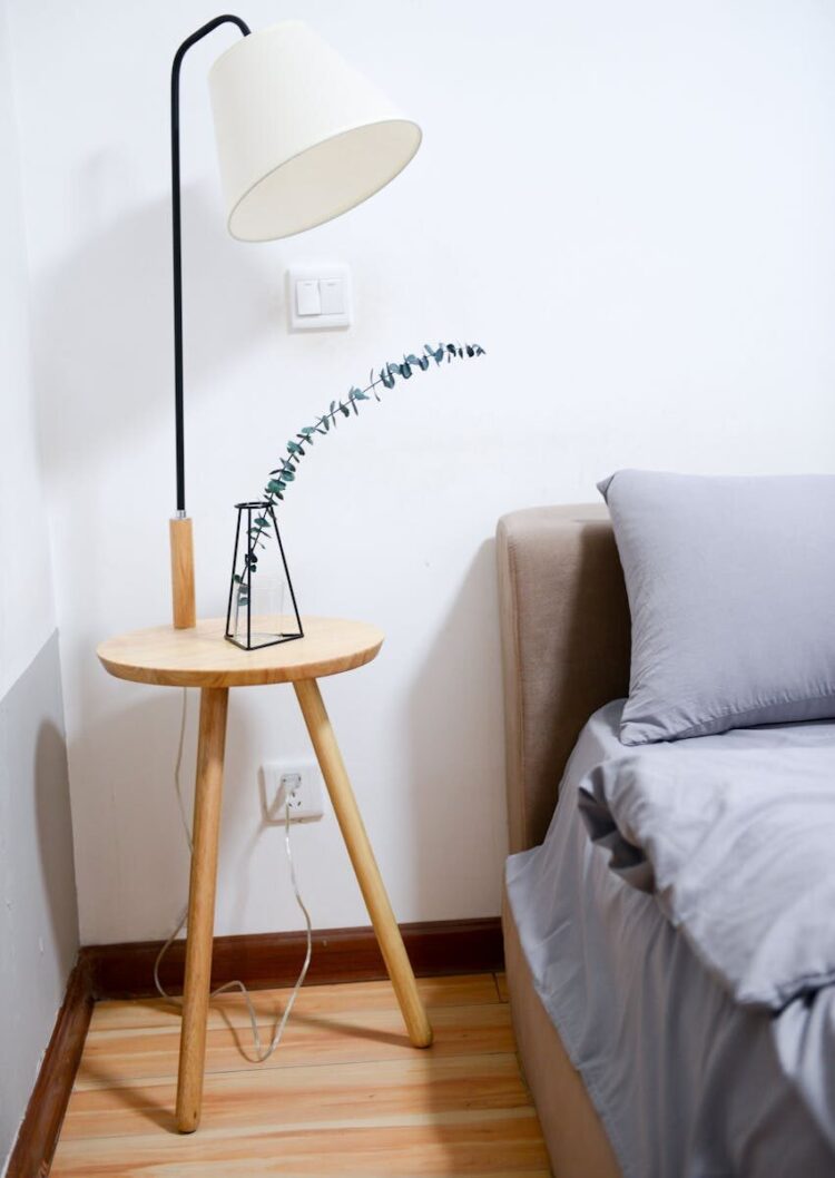 Modern minimalist bedroom with wooden nightstand, sleek lamp, and gray bedding set.