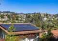 Solar panels on a suburban home, surrounded by lush greenery and a sunny blue sky.