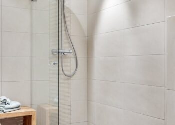 Elegant modern bathroom featuring a glass shower and minimalist design with neutral tiles and wooden accents.