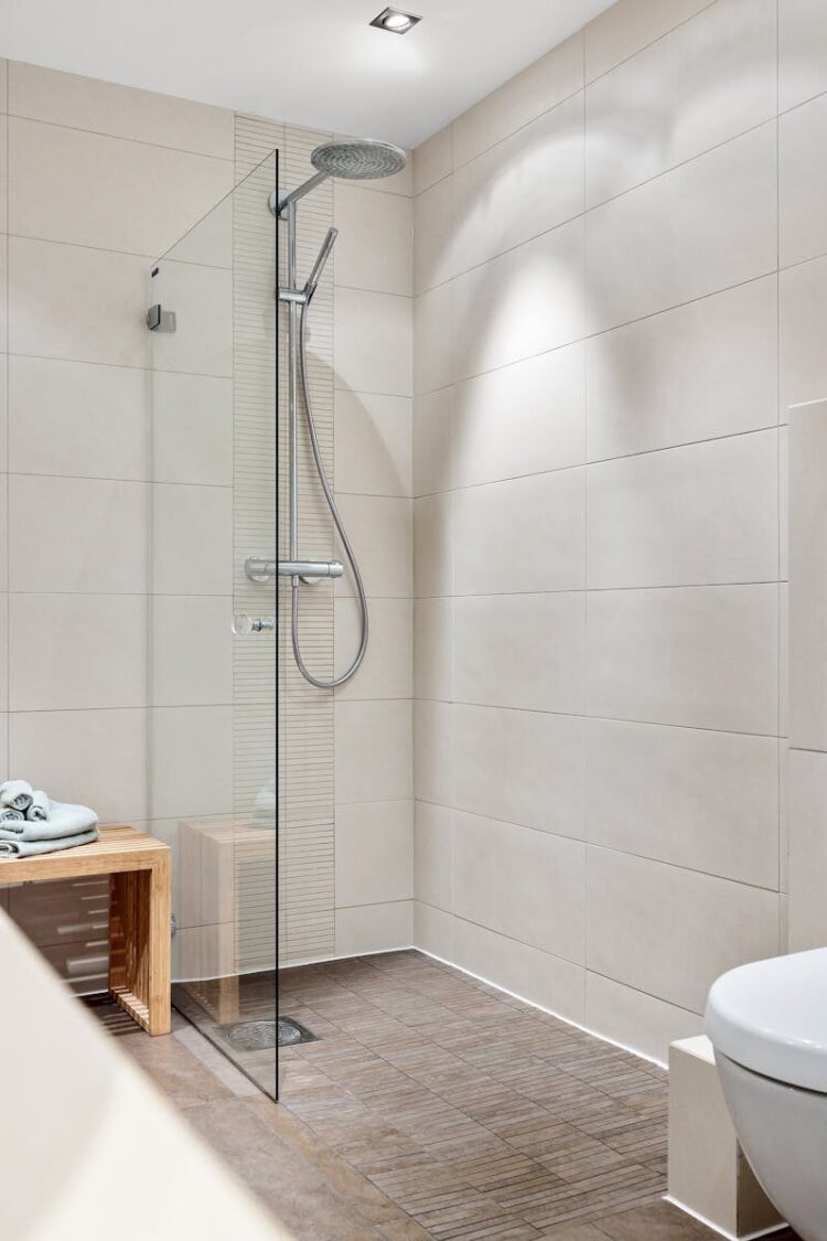 Elegant modern bathroom featuring a glass shower and minimalist design with neutral tiles and wooden accents.