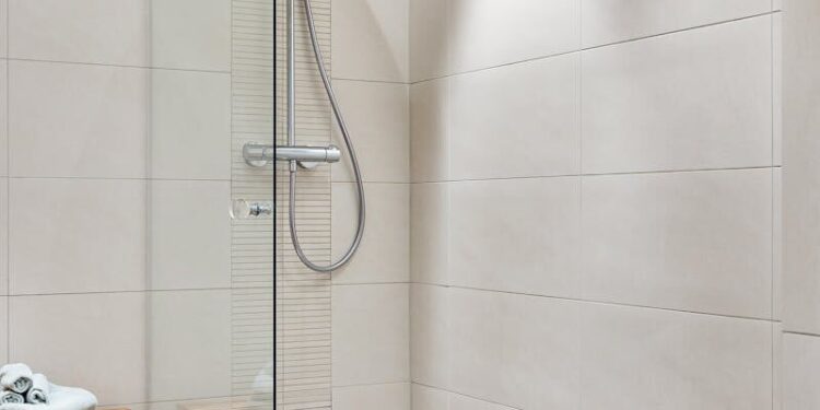 Elegant modern bathroom featuring a glass shower and minimalist design with neutral tiles and wooden accents.