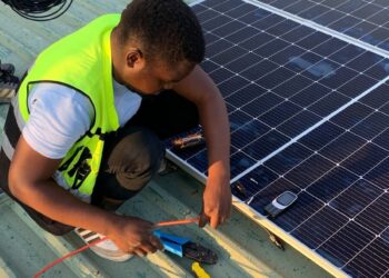 Technician working on solar panel installation with cables and tools on a sunny day.