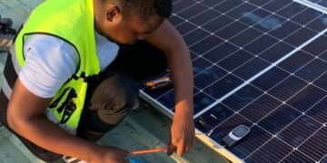 Technician working on solar panel installation with cables and tools on a sunny day.