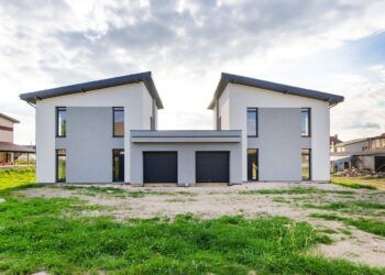 Front view of twin modern houses with a symmetrical architectural design under a cloudy sky.