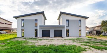 Front view of twin modern houses with a symmetrical architectural design under a cloudy sky.
