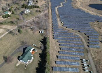 Aerial image showcasing a solar farm adjacent to a residential area in a rural setting.