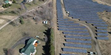 Aerial image showcasing a solar farm adjacent to a residential area in a rural setting.
