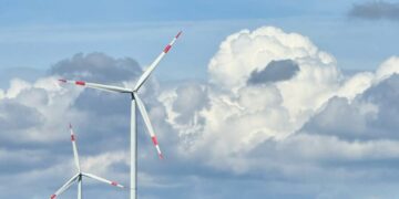 Two wind turbines in a countryside setting with a dramatic cloudy sky.