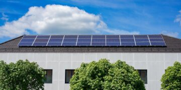 Energy-efficient building topped with solar panels and surrounded by lush trees.