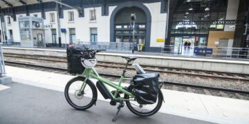 A green cargo bike parked at a railway station platform in France, highlighting sustainable travel.