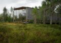 A contemporary wooden cabin with glass facade nestled in a forest landscape.