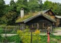 Charming wooden cabin with a turf roof surrounded by lush greenery.