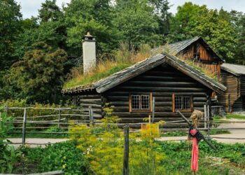 Charming wooden cabin with a turf roof surrounded by lush greenery.