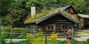 Charming wooden cabin with a turf roof surrounded by lush greenery.