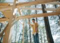 Asian man at a construction site building a wooden frame among trees.