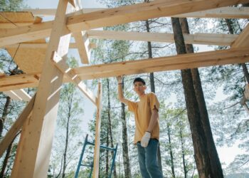 Asian man at a construction site building a wooden frame among trees.